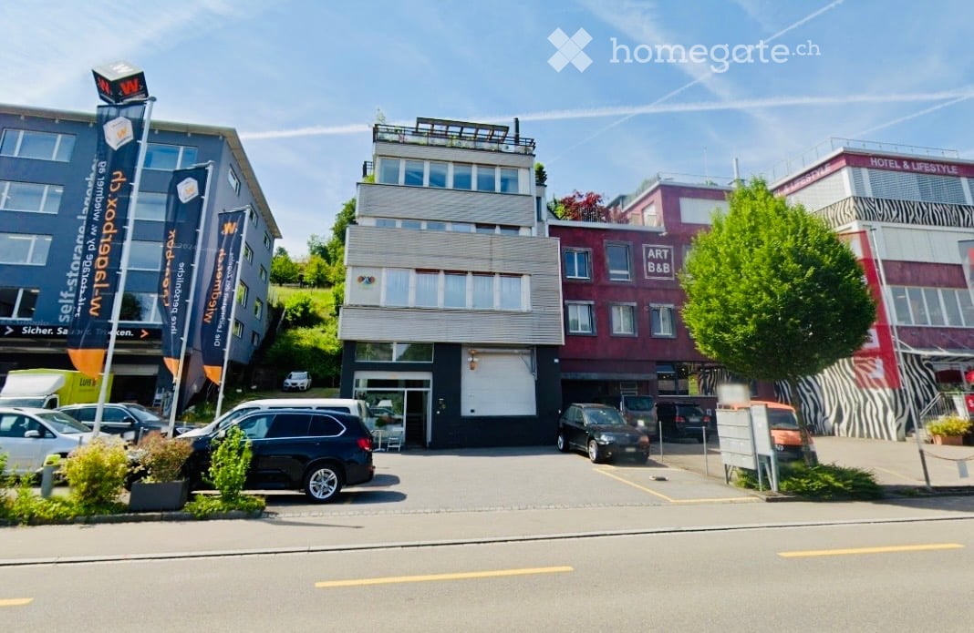 A multi-story commercial building with modern architecture, featuring large windows, signage for 'selfstorage', and a parking area with several cars.