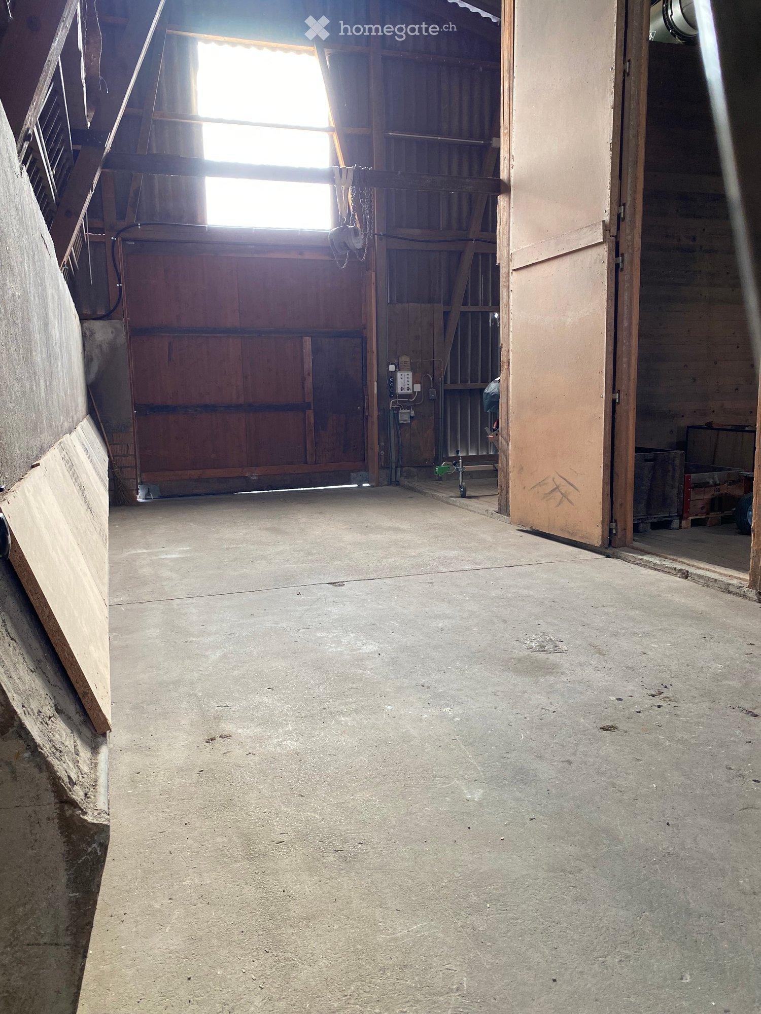 Empty barn interior with concrete floor, wooden walls, and large open doors allowing natural light to enter.