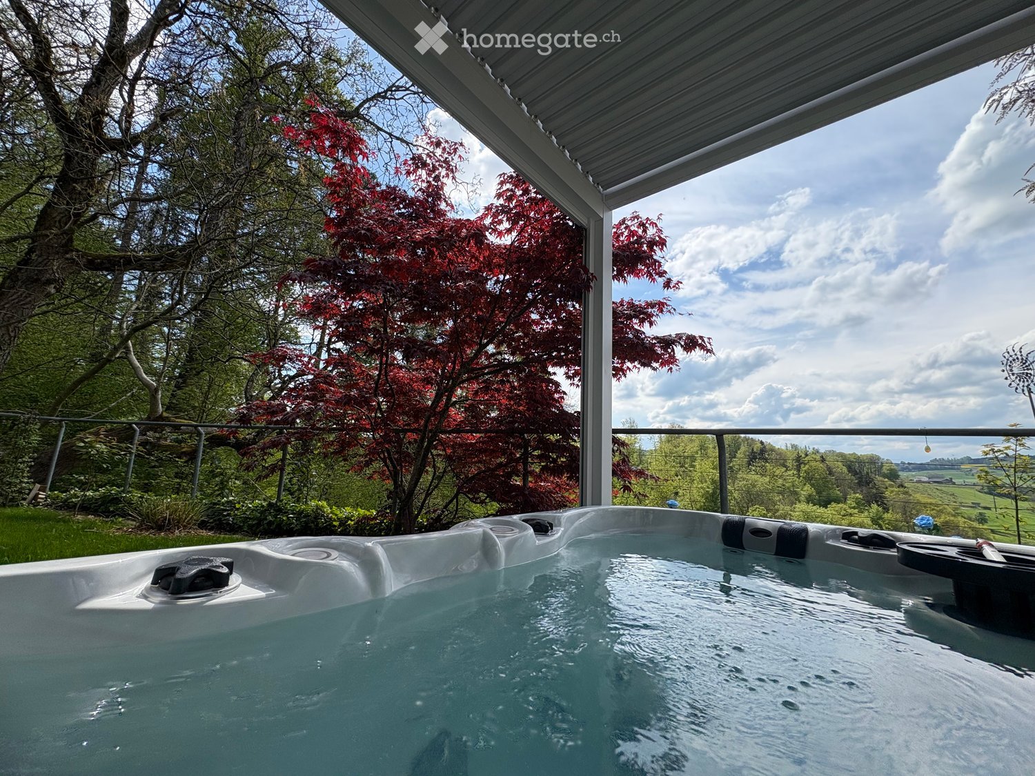 A hot tub on a covered outdoor patio with a scenic view of a garden and countryside.