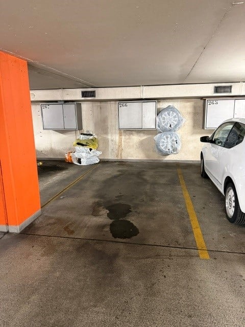 Underground parking space with a white car parked, marked parking spots, and storage cabinets on the wall.