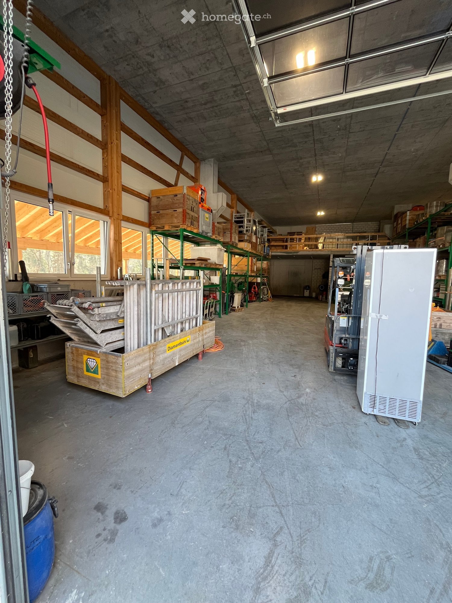 Industrial warehouse with high ceilings, concrete floors, wooden pallets, metal shelves, industrial equipment, large windows, and a forklift.