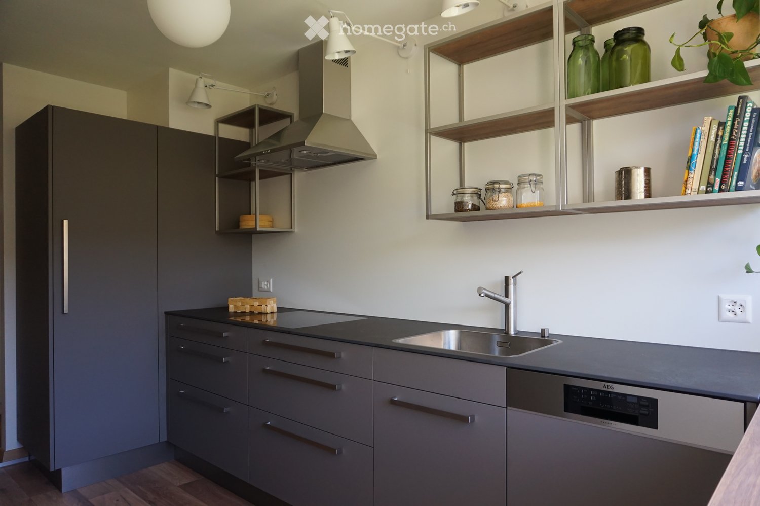 Kitchen. Modern kitchen with grey cabinets, stainless steel sink, dishwasher, and open shelving with jars and books.