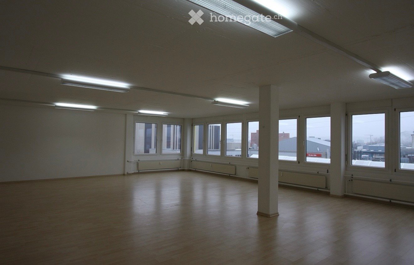 Unfurnished Room. Empty room with wooden flooring, white walls, large windows, and fluorescent lighting.