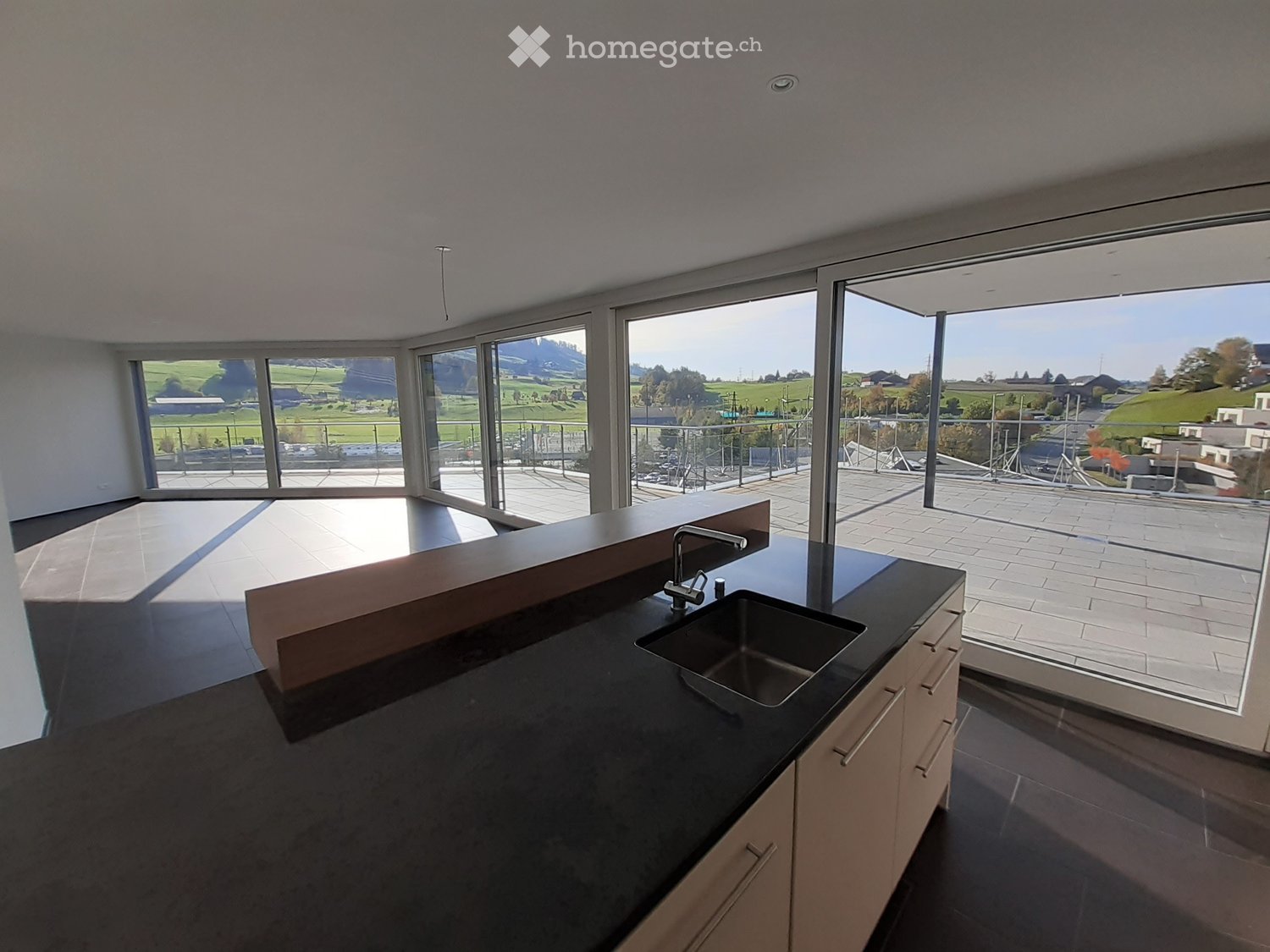Modern kitchen with black countertop, stainless steel sink, and light-colored cabinets, featuring large windows overlooking a scenic landscape.