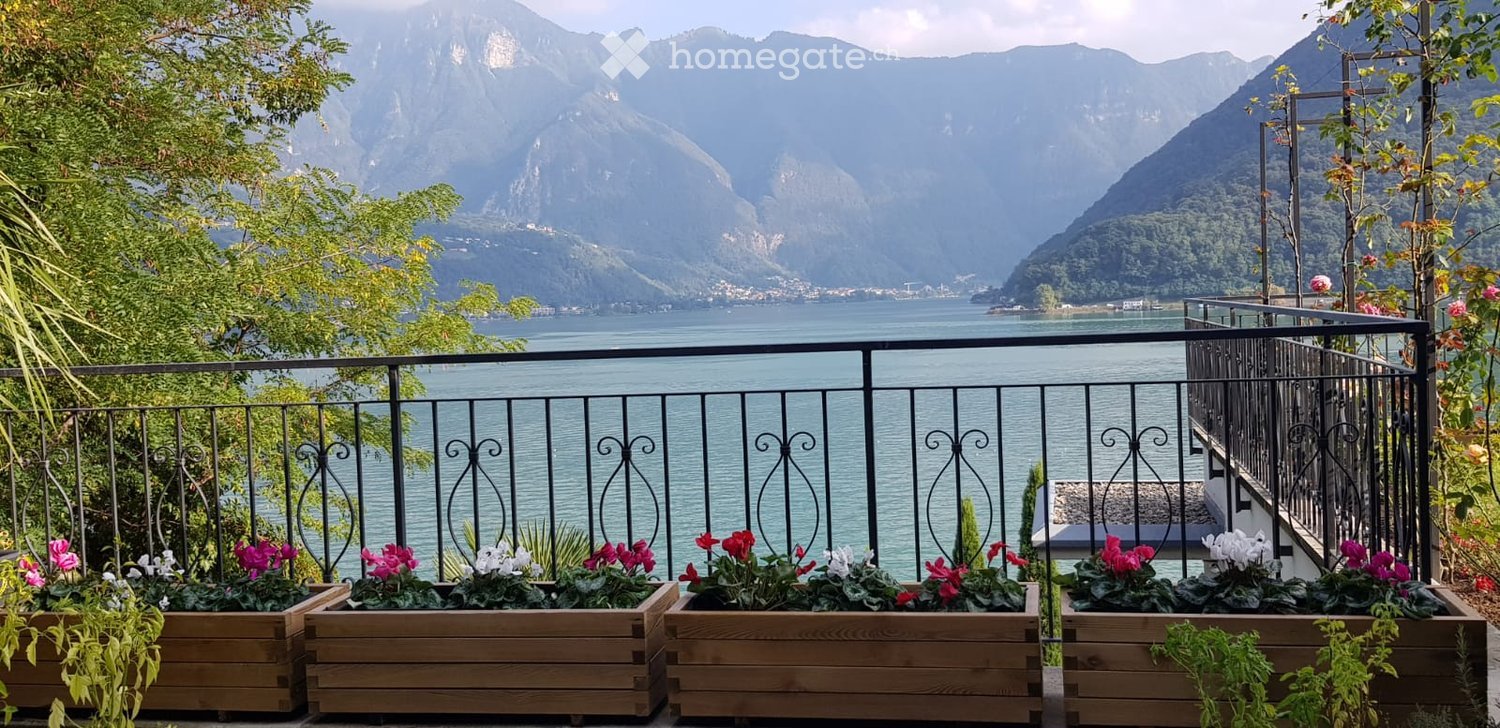 Balcony with wooden planters filled with colorful flowers, overlooking a scenic lake and mountain backdrop.