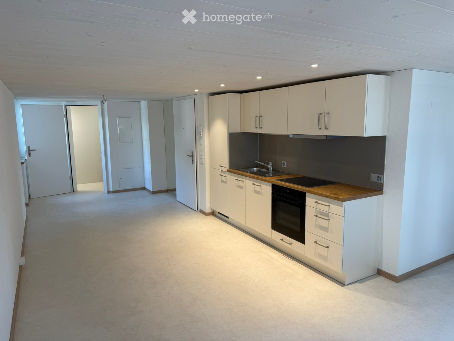 Modern kitchen with white cabinets, wooden countertops, sink, faucet, and oven. Open space with carpeted floor and recessed lighting.