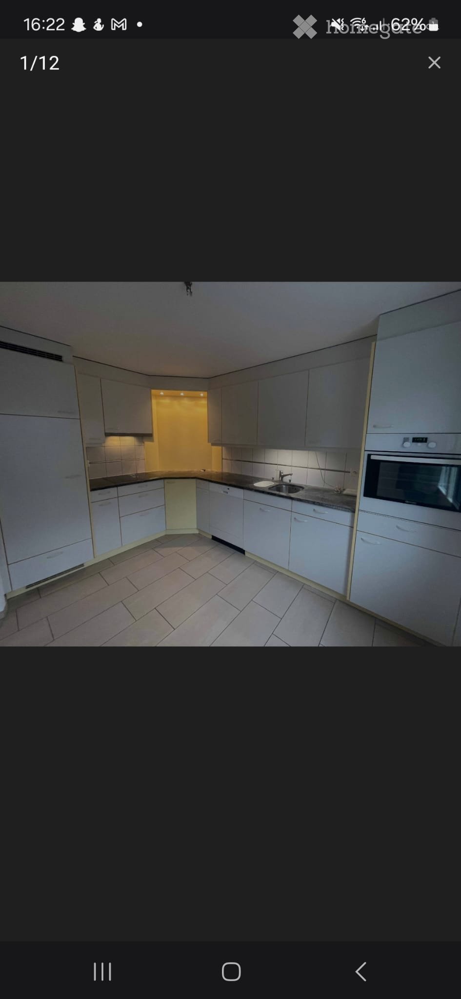 Modern kitchen with white cabinets, a sink, and an oven, featuring tiled flooring and warm lighting.