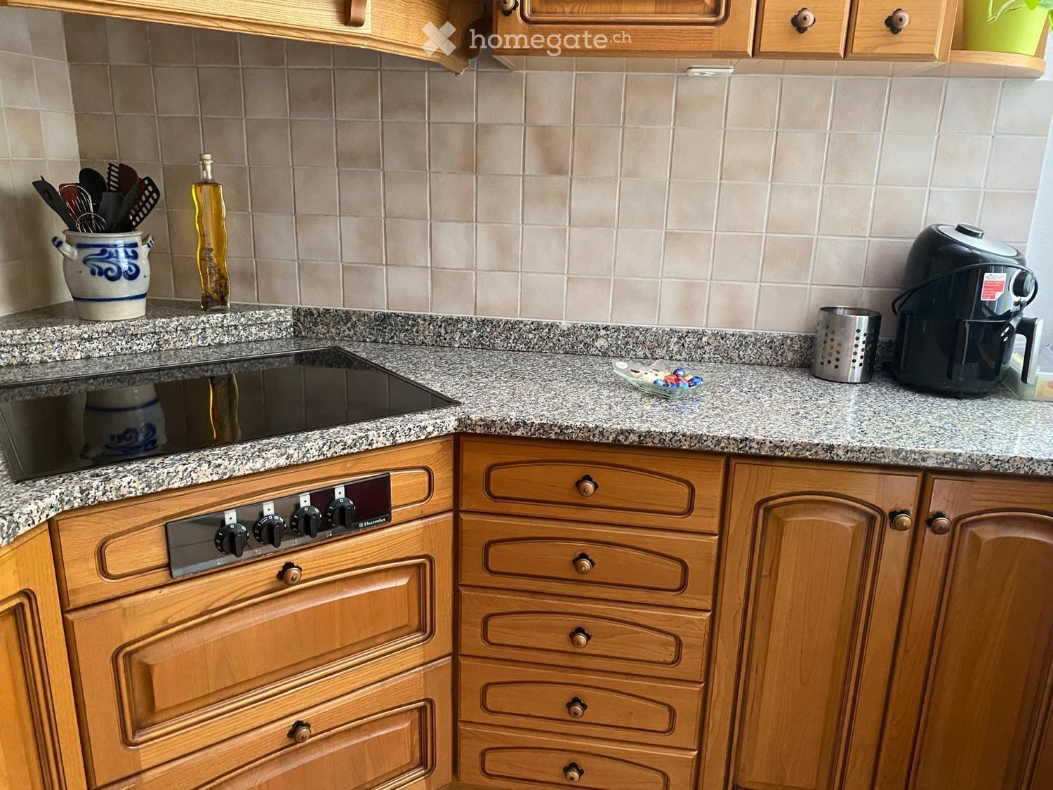 kitchen with granite countertop, wooden cabinets, black induction stove, black air fryer, stainless steel strainer, oil bottle, and a blue and white ceramic jar