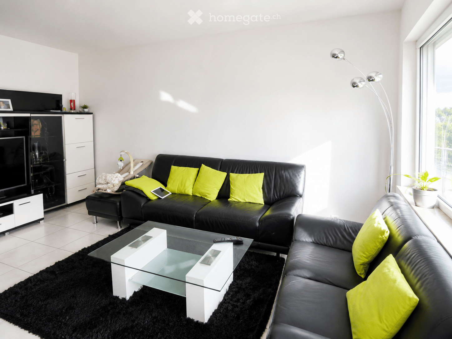 Modern living room with black leather sofas, bright yellow cushions, a glass coffee table, a black shag rug, and a sleek TV stand.