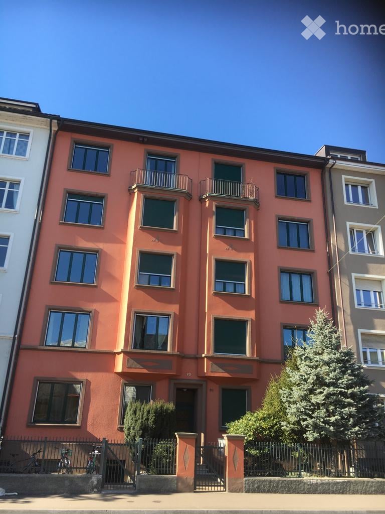 Four-story apartment building with orange facade, multiple windows, and balconies on the upper floors.