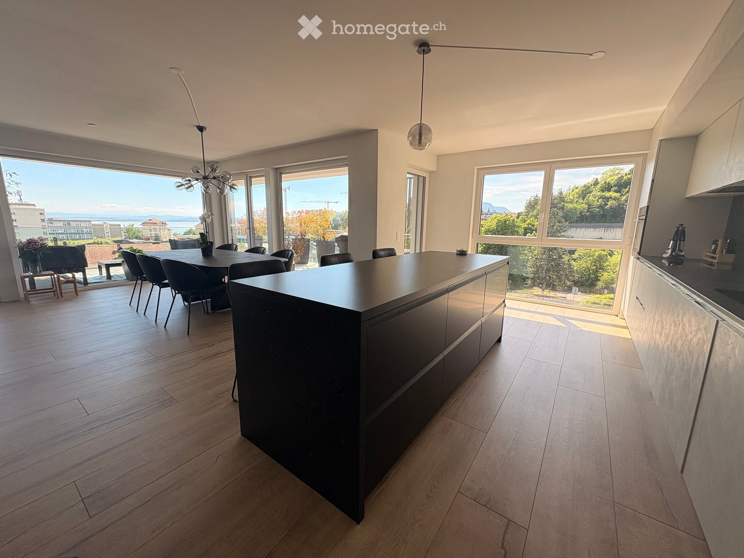 Modern kitchen with a central island, dining area, pendant lights, and large windows offering a scenic view.