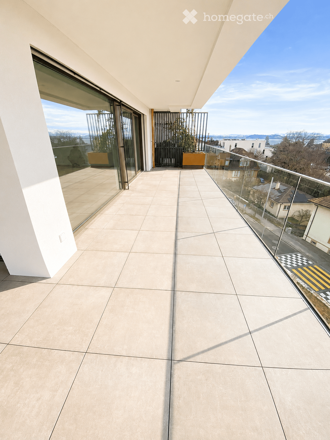 Modern balcony with large glass railings, tiled floor, and scenic city view.