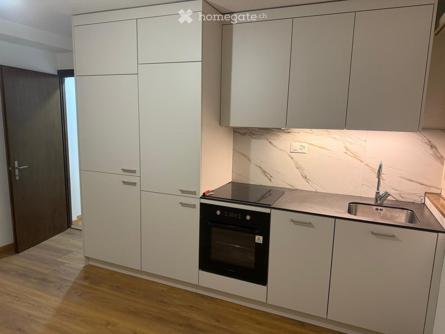 Modern kitchen with white cabinets, marble backsplash, wooden flooring, and stainless steel sink and oven.