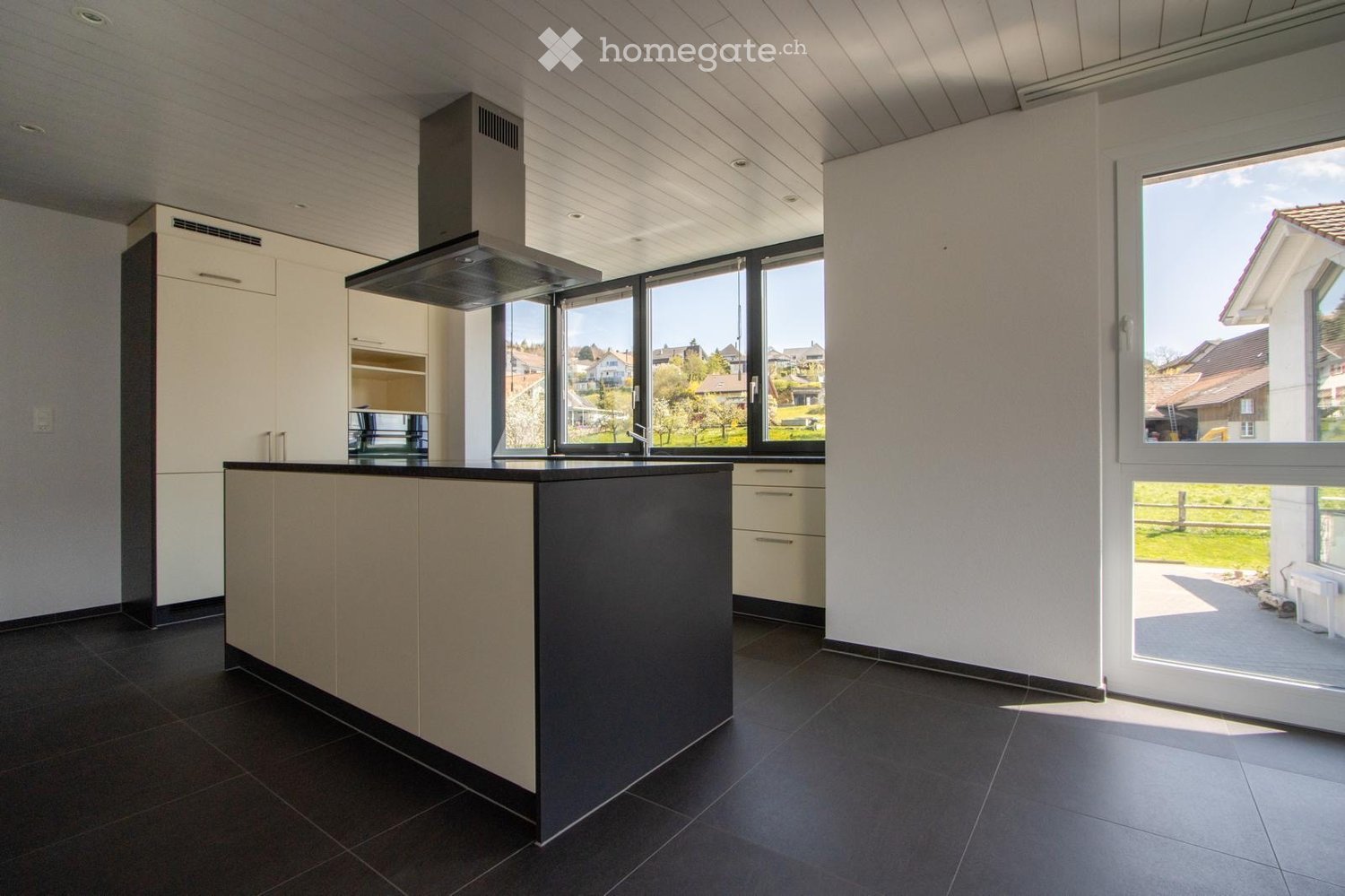 Modern kitchen with a central island, white cabinets, dark countertops, and large windows offering a view of the surrounding area.