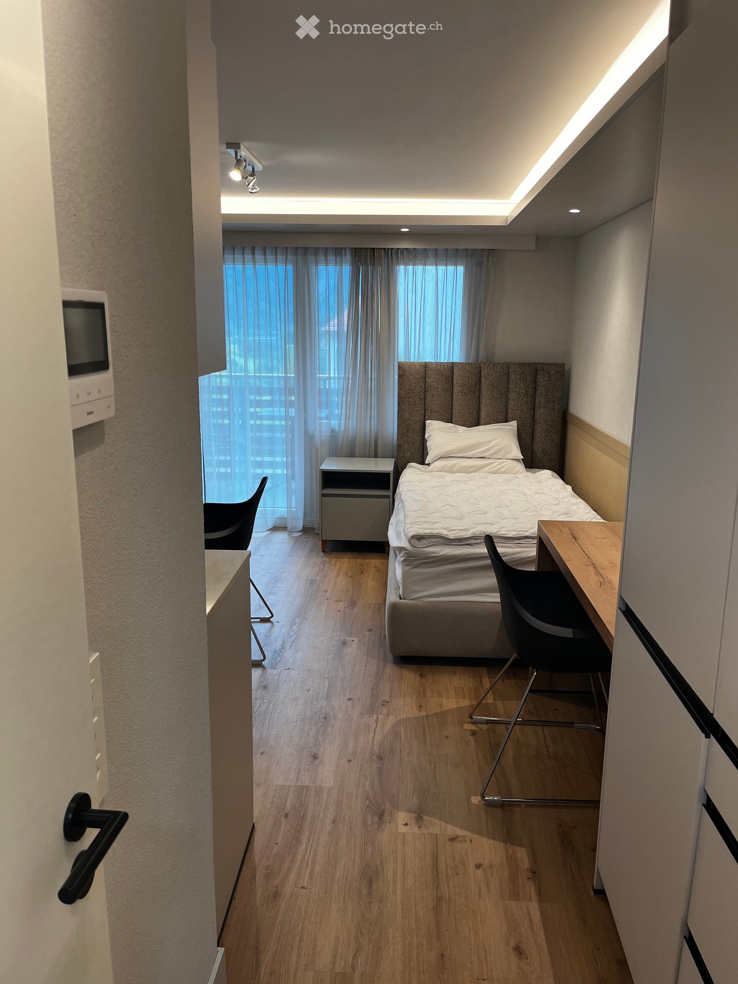 single bed, wooden floor, large windows, ceiling lights, desk, 2 chairs, small cabinet