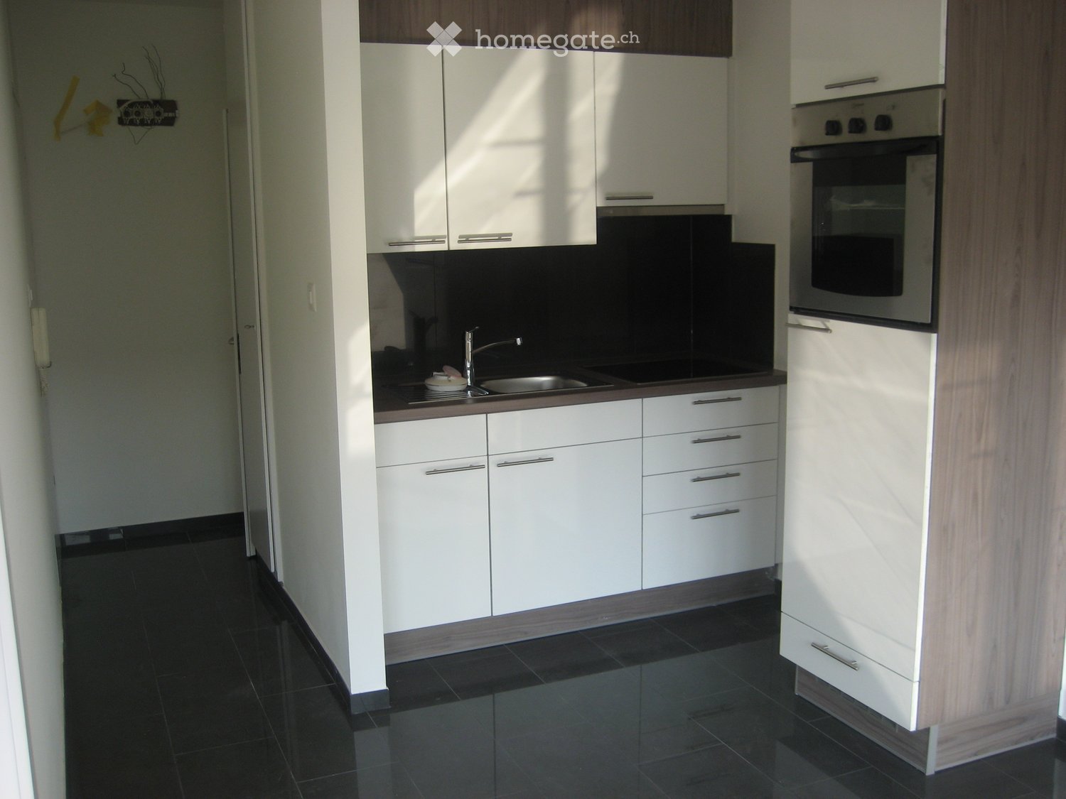 Modern kitchen with white cabinets, black tiled floor, stainless steel sink, and built-in oven.