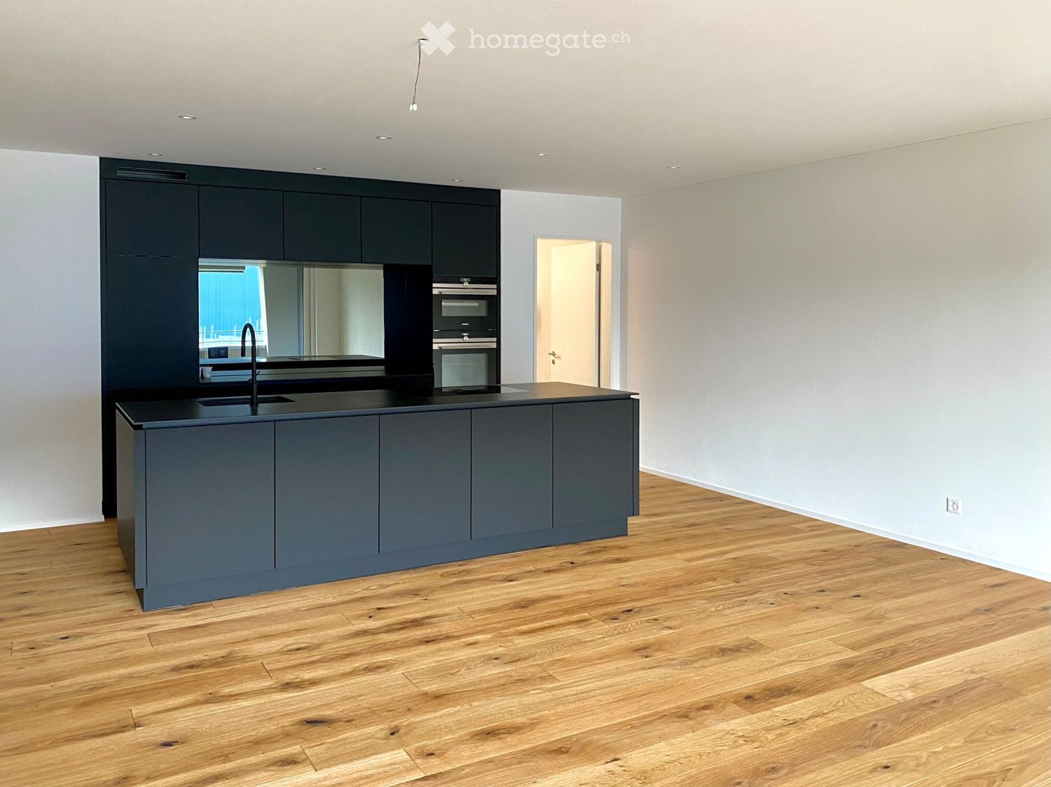 Modern kitchen with dark grey cabinets, a central island, and a black countertop. Features a sink, faucet, and built-in oven.