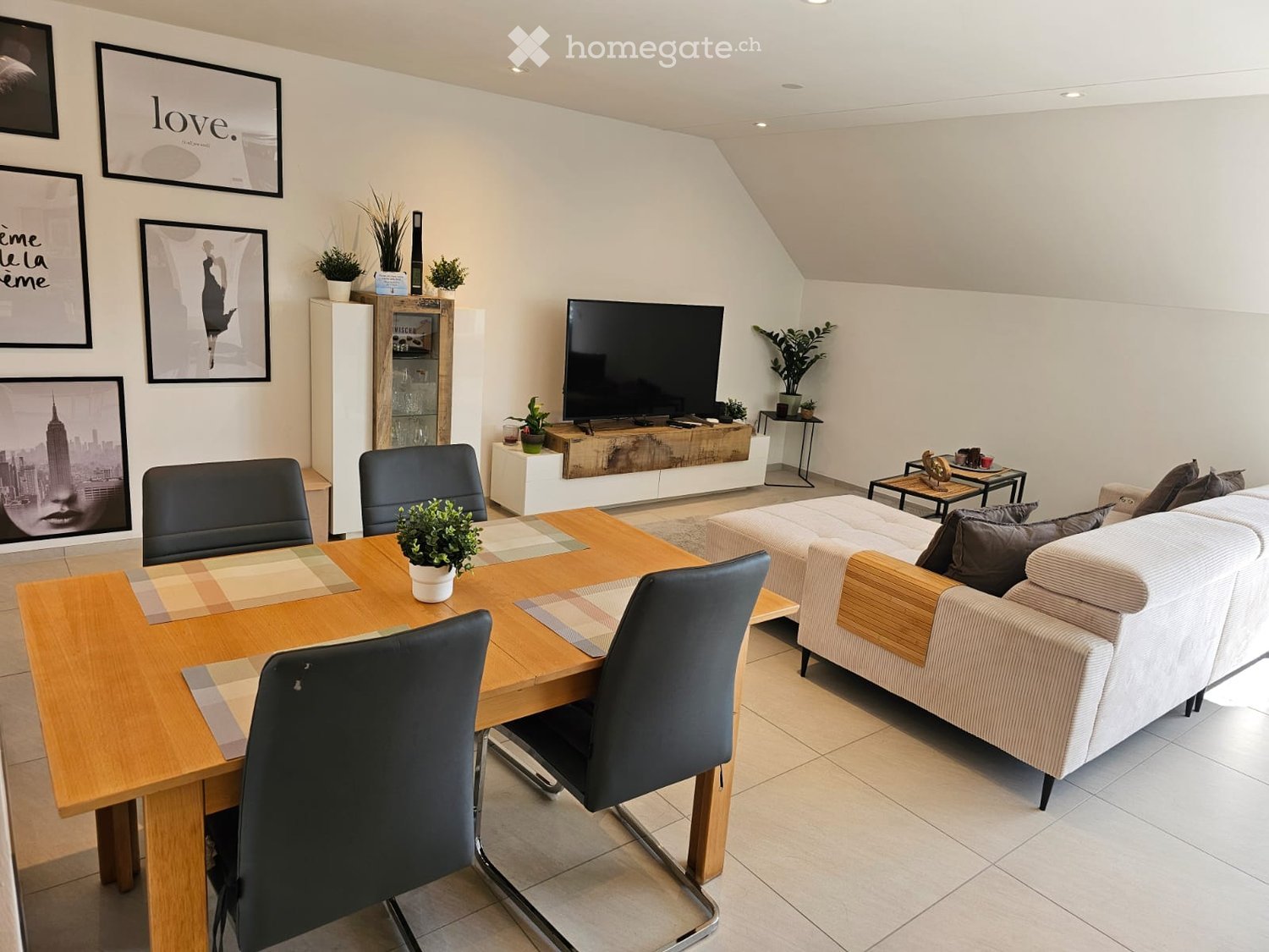 Modern living room with a white sofa, coffee table, dining table with chairs, television, and decorative plants.