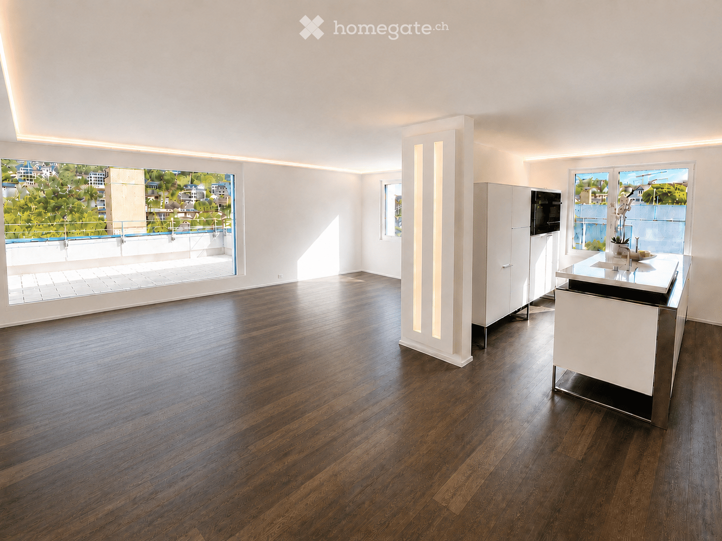 Open-plan unfurnished room with wooden flooring, white walls, and large windows offering a view of a cityscape. Features include built-in cabinets, a modern kitchen island, and recessed lighting.