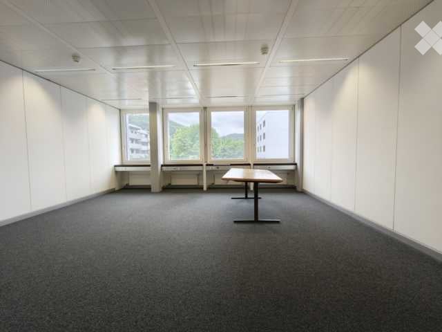 Empty room with white walls, carpeted floor, large windows, and a single table in the center.