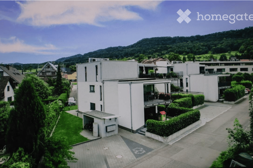 Modern multi-story residential building with white exterior, balconies, garage, and parking area.