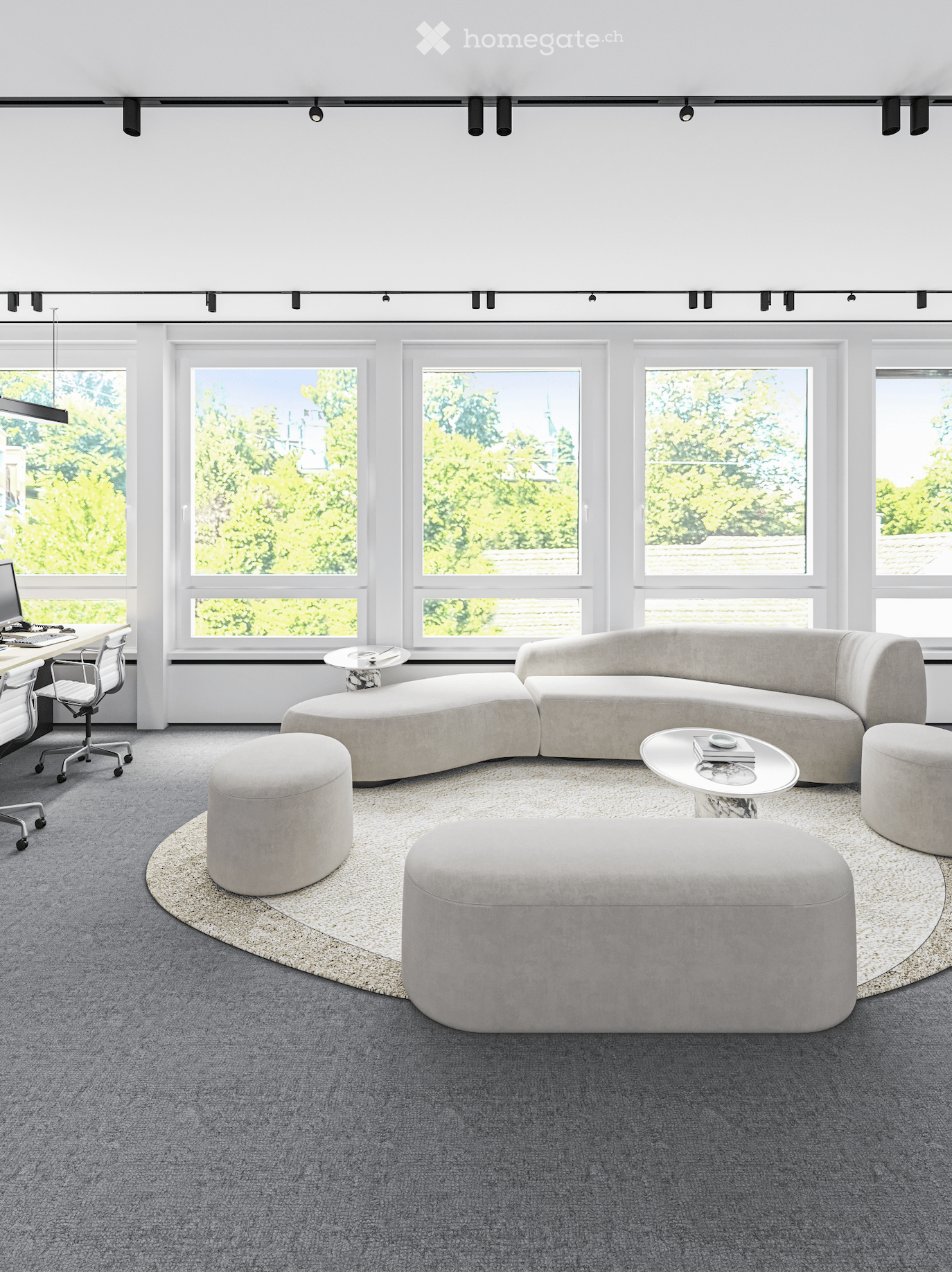 Modern living room with large windows, grey sectional sofa, round ottomans, small tables, and a computer desk with chair.