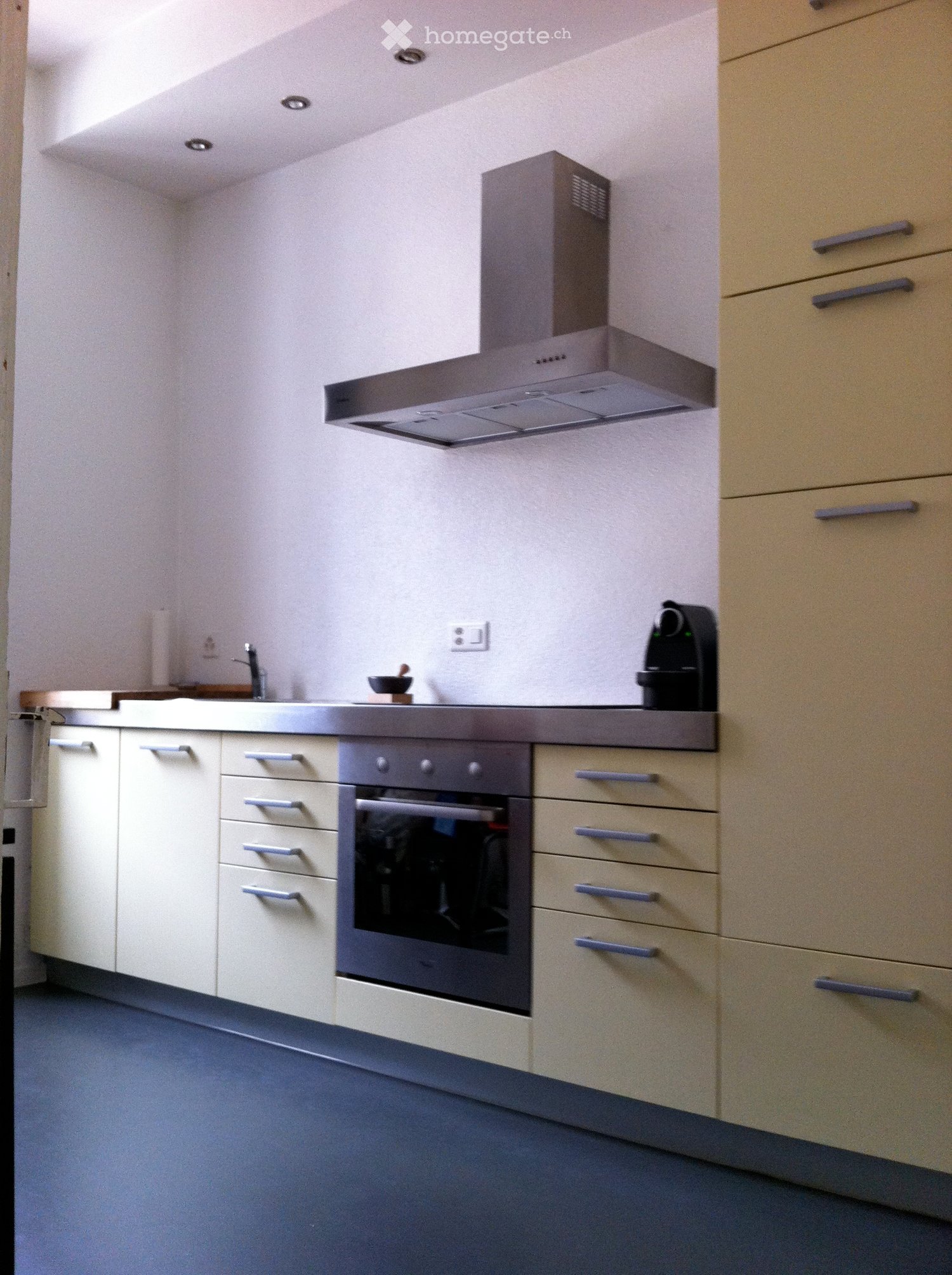 Modern kitchen with white cabinets, grey countertops, built-in oven, and a coffee machine on the counter.