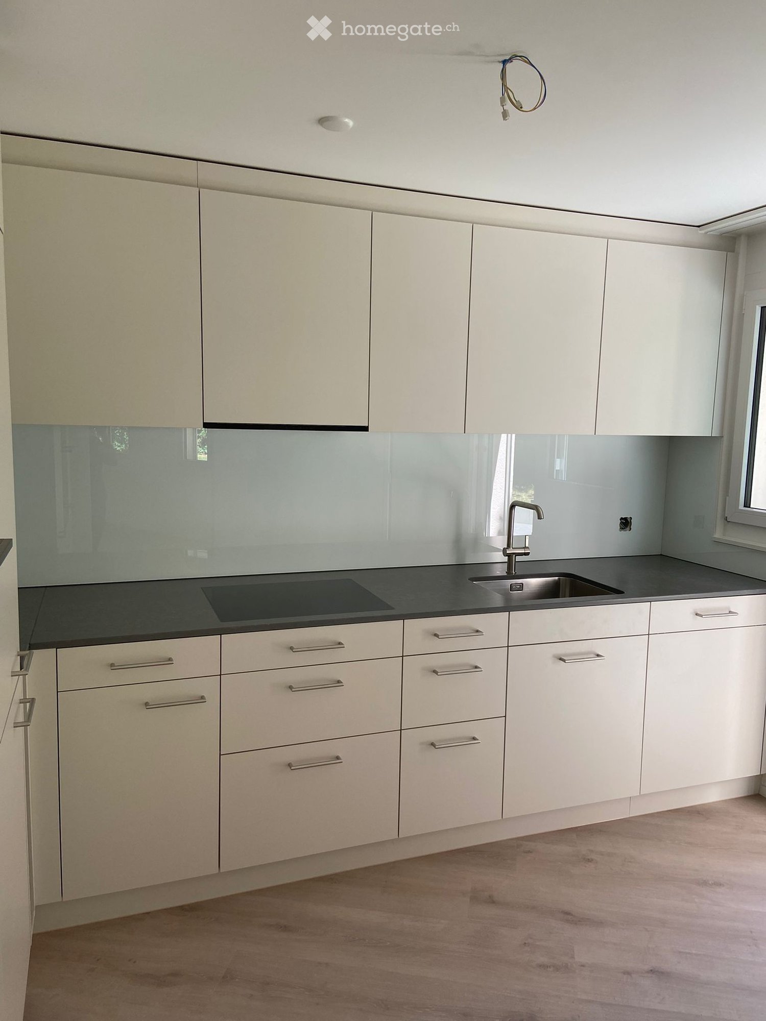 Modern kitchen with white cabinets, stainless steel handles, a black countertop, and a built-in stove. Features a sleek, minimalist design with a glass backsplash.
