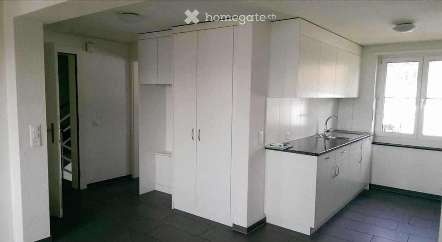 Modern kitchen with white cabinets, a sink, and a faucet. The space is clean and organized with a dark tiled floor and a window providing natural light.