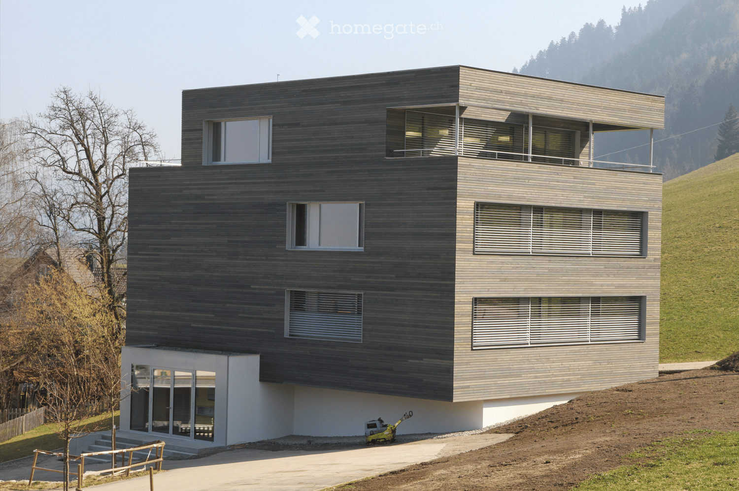 modern house, 3 levels, dark gray wooden facade, windows with white shutters, balconies
