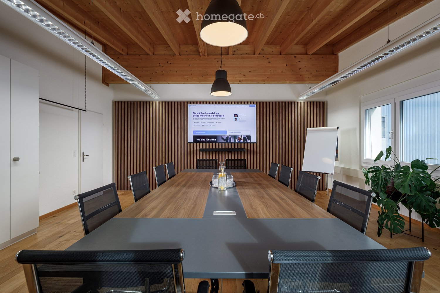 conference room with a long table, chairs, a whiteboard, a monitor, and a wooden wall