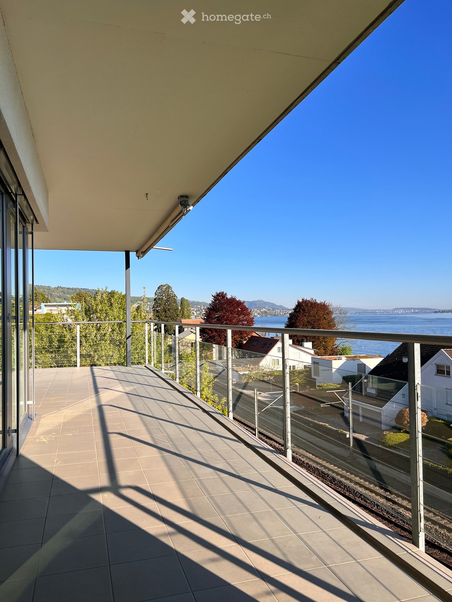 Balcony with tiled floor, glass railing, and scenic view of water and surrounding landscape.