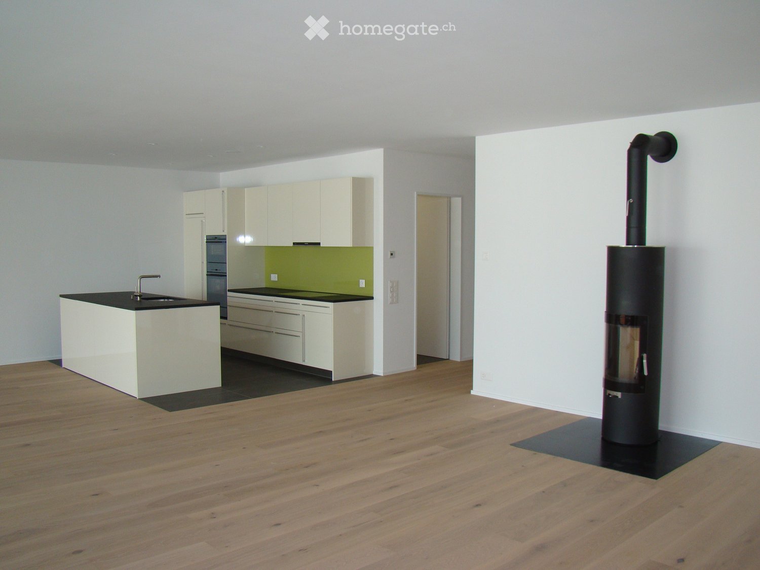 Modern kitchen with white cabinets, black countertops, and a central island. A wood-burning stove is positioned near the wall.