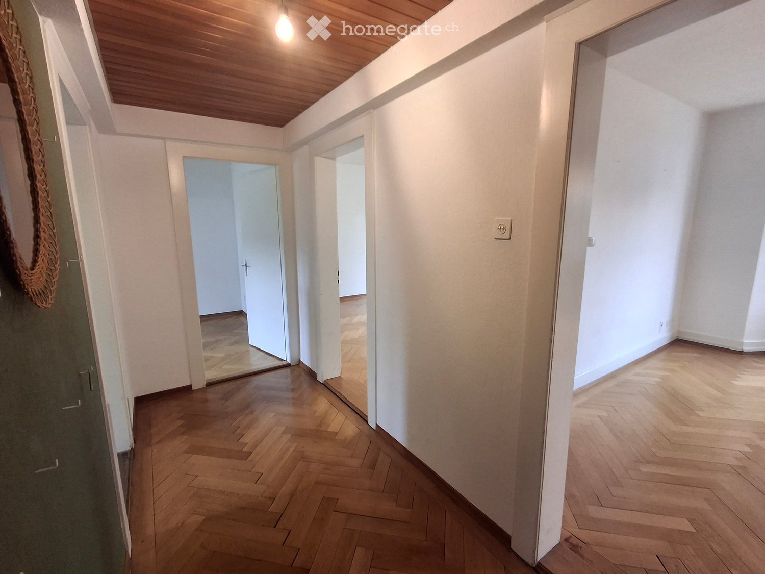Empty hallway with wooden flooring, white walls, and open doors leading to other rooms.