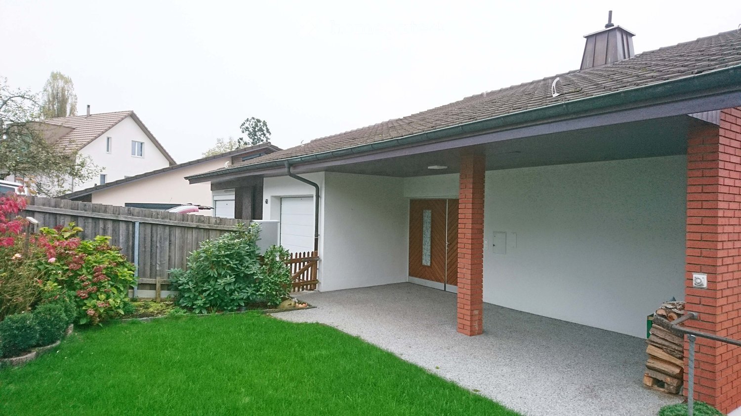 Well-maintained garden with green lawn, wooden fence, and brick house entrance.