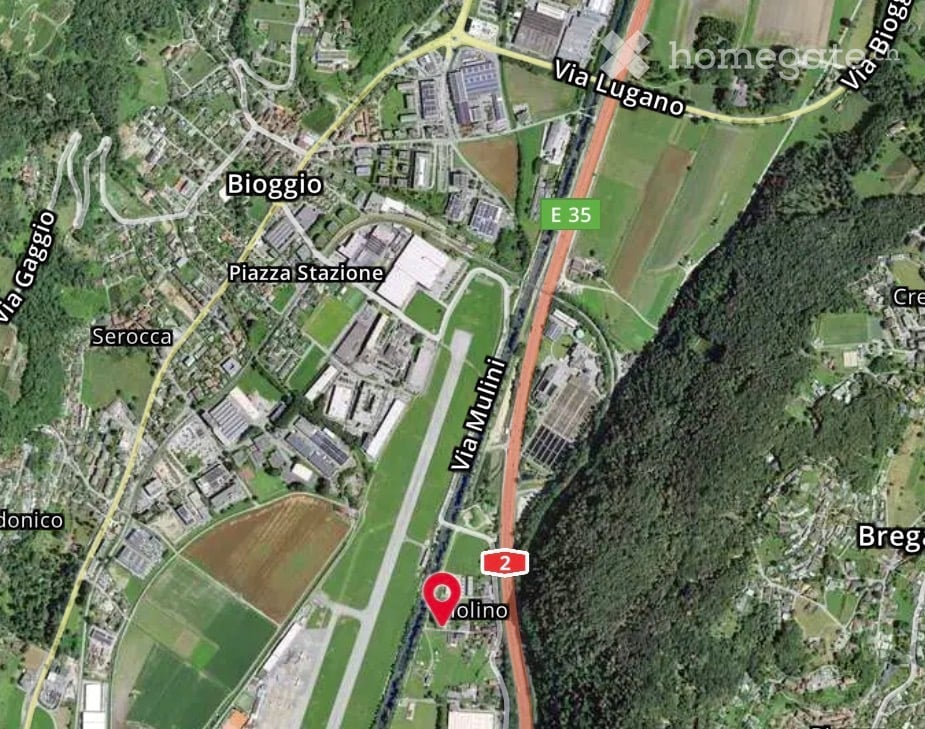 Aerial view of a suburban area showing roads, buildings, and green spaces. Key locations labeled include Bioggio, Piazza Stazione, Serocca, and Olino.
