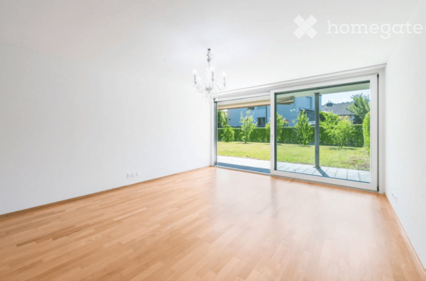 Empty room with light wooden flooring, white walls, and large sliding glass doors leading to a garden area.