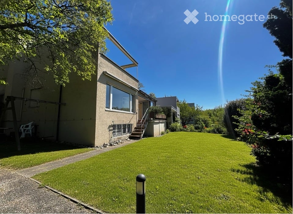 Modern house with a well-maintained garden, featuring a large lawn, a swing, and a pathway leading to the entrance.