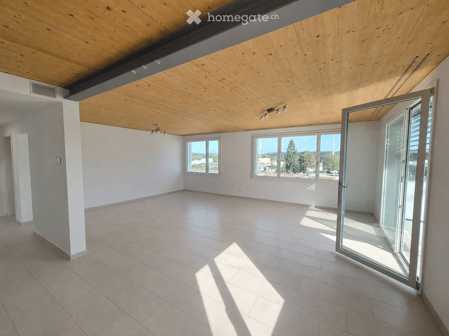 Empty room with light wooden ceiling, tiled floor, white walls, large windows, and a sliding glass door leading outside.