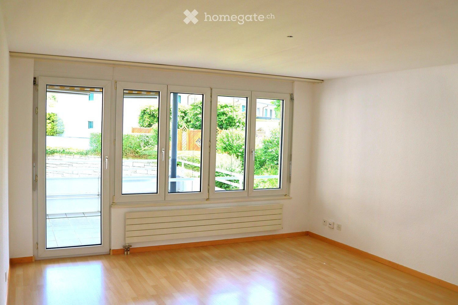 Empty room with wooden flooring, white walls, large windows, and a radiator. No furniture or equipment present.