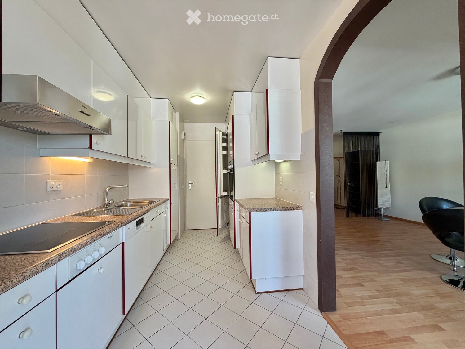 Modern kitchen with white cabinets, granite countertops, stainless steel appliances, and a small seating area with a black chair.