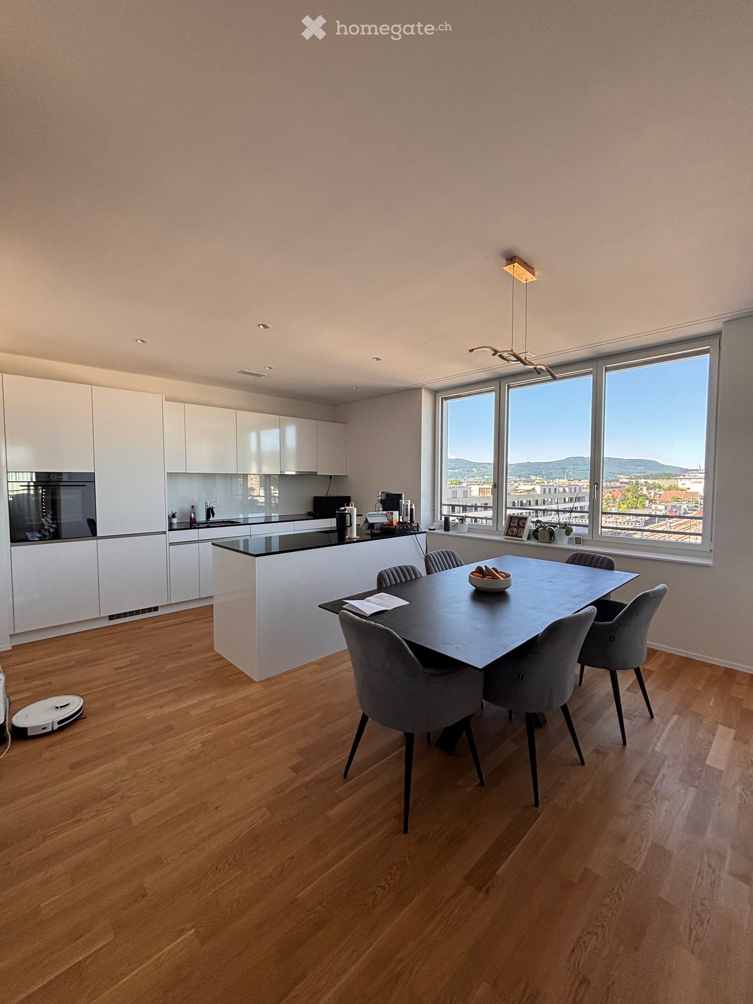 Modern kitchen and dining area with white cabinets, black countertops, a large dining table with six chairs, and a view of the cityscape through large windows.