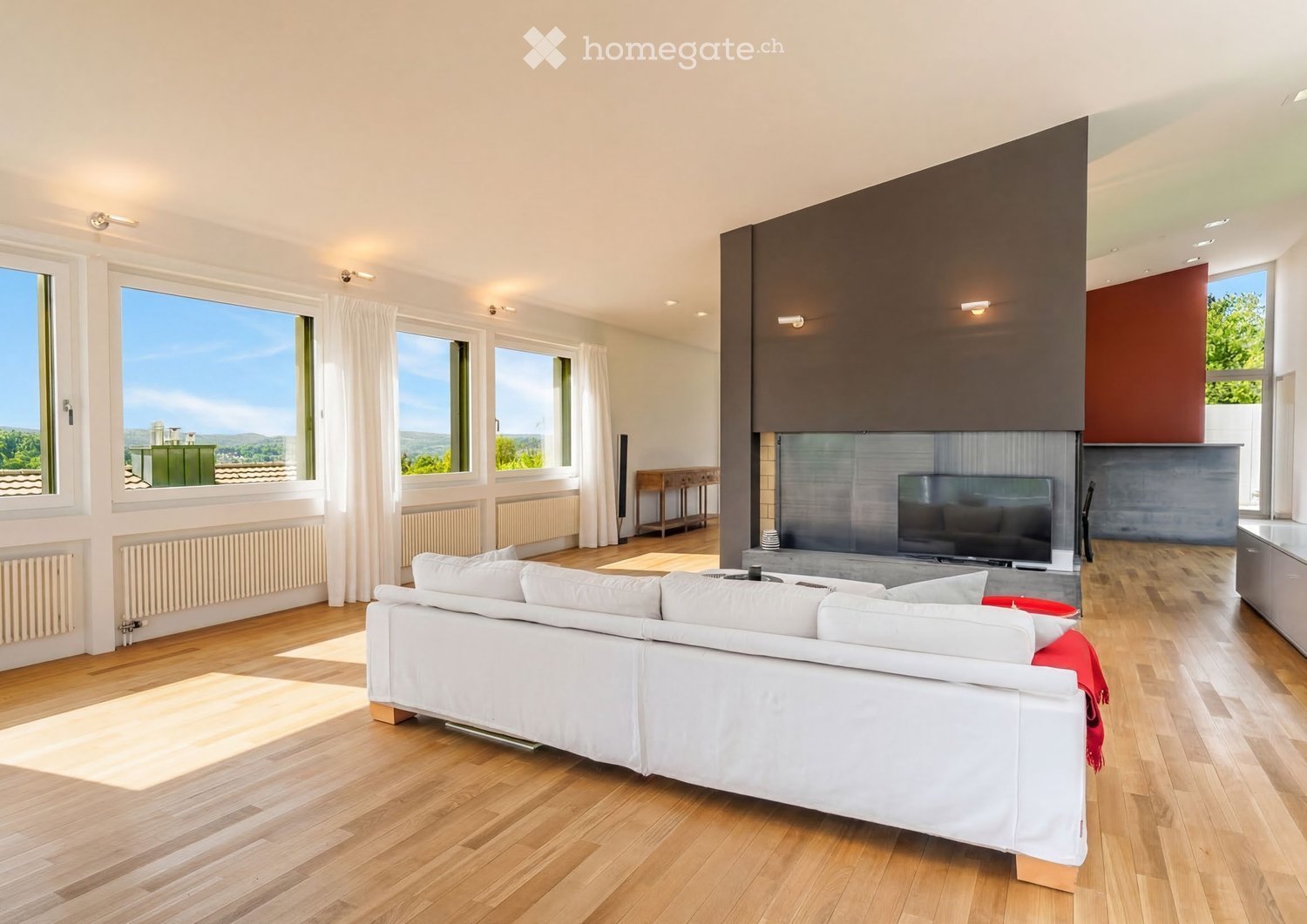 Modern living room with large windows offering a scenic view, a white sofa, a coffee table, a television, and a small table with chairs.