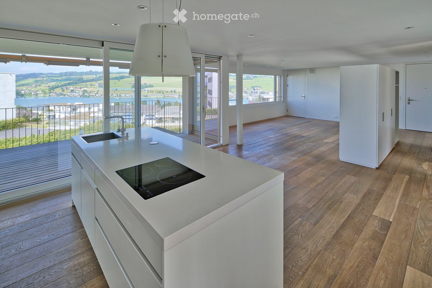 Modern kitchen with white island, induction cooktop, sink, pendant light, and large windows offering a scenic view.