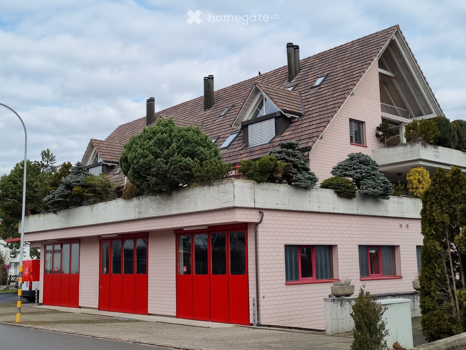 Two-story house with pink brick facade, red garage doors, multiple windows, and a balcony on the upper level.