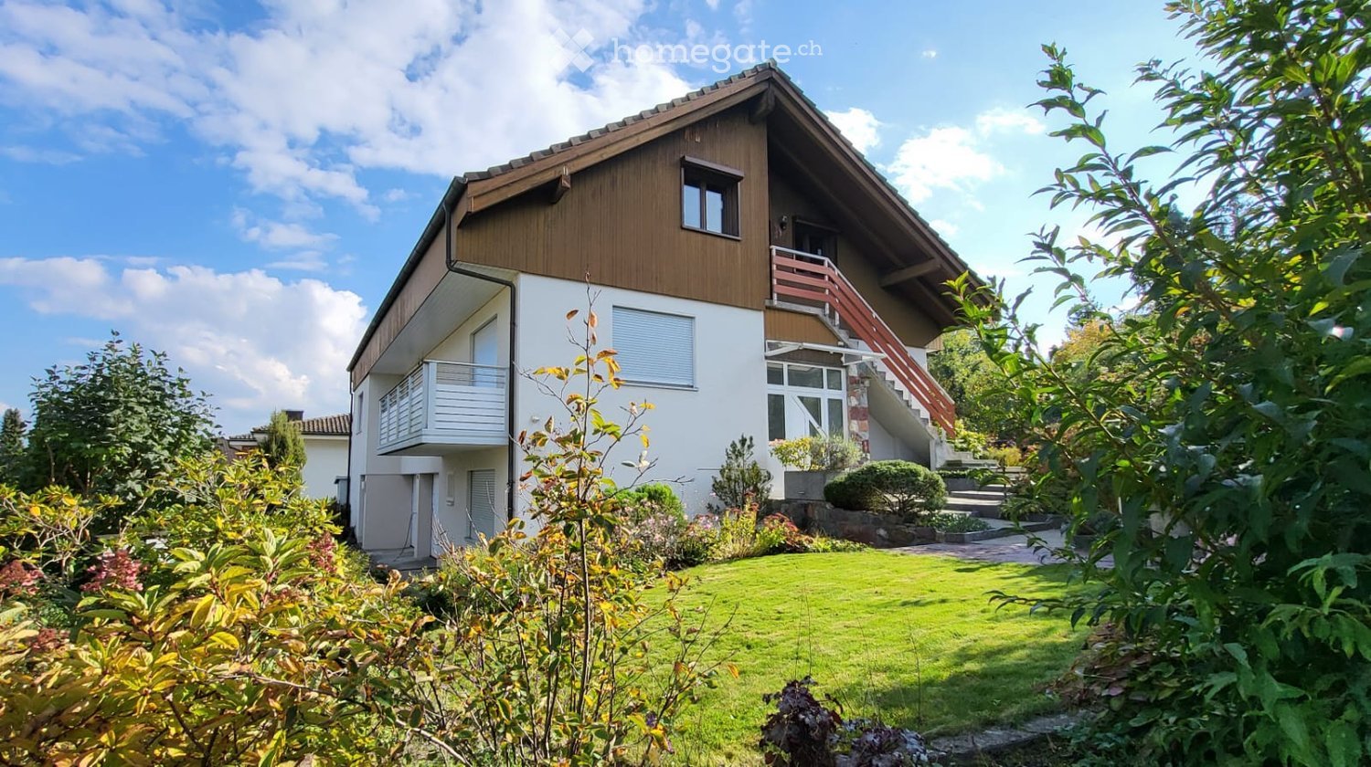 Two-story house with a wooden facade, white walls, and a well-maintained garden with green lawn and various plants.