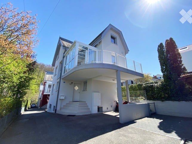 House. Modern two-story house with a large balcony and garage, surrounded by greenery.