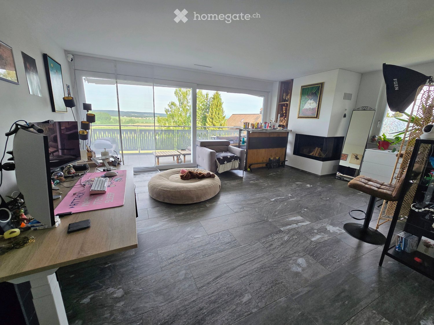 Modern living room with large windows offering a scenic view, featuring a sofa, coffee table, fireplace, and various decorative items.