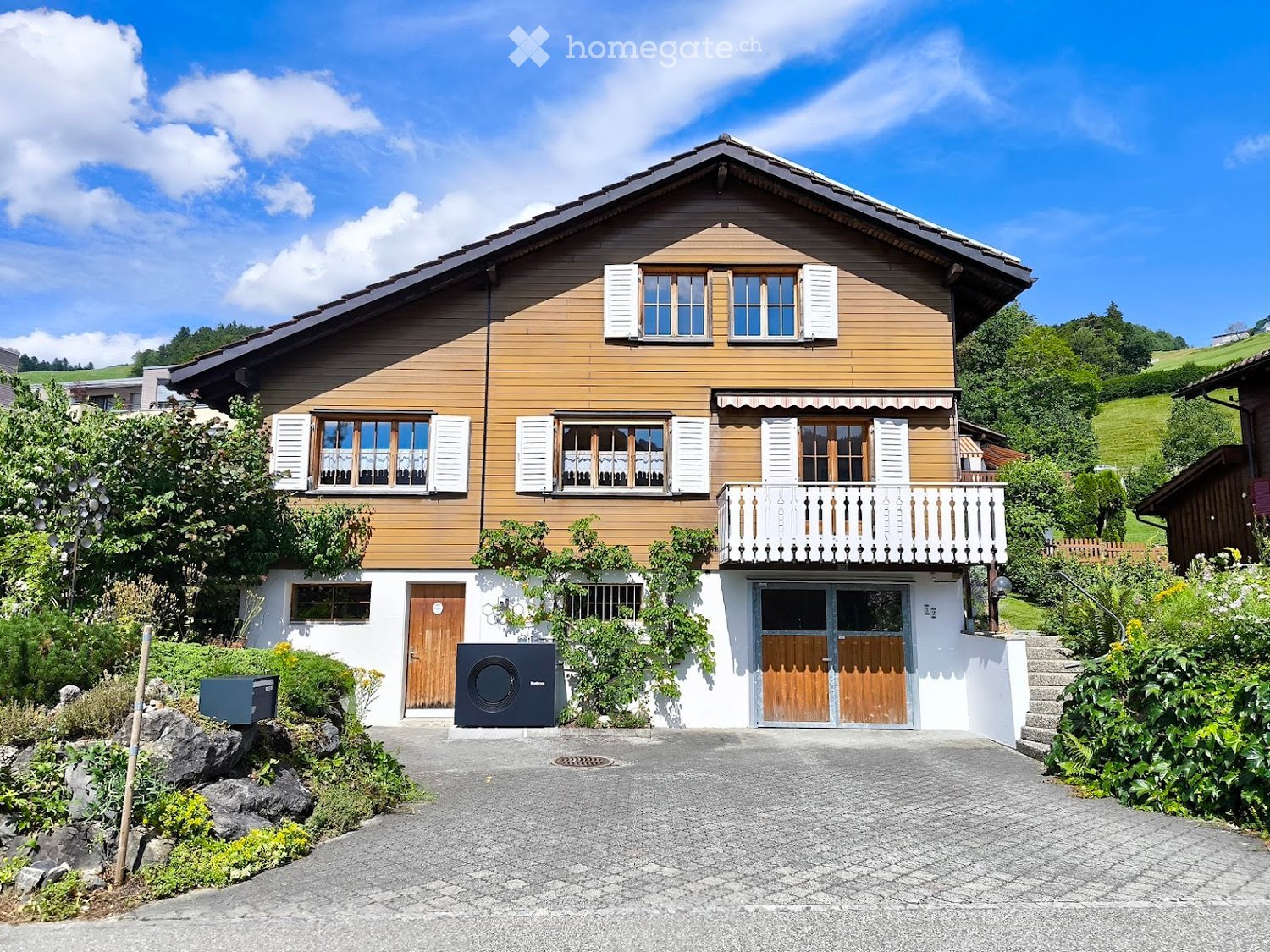 Two-story wooden house with white shutters, balcony, and driveway.