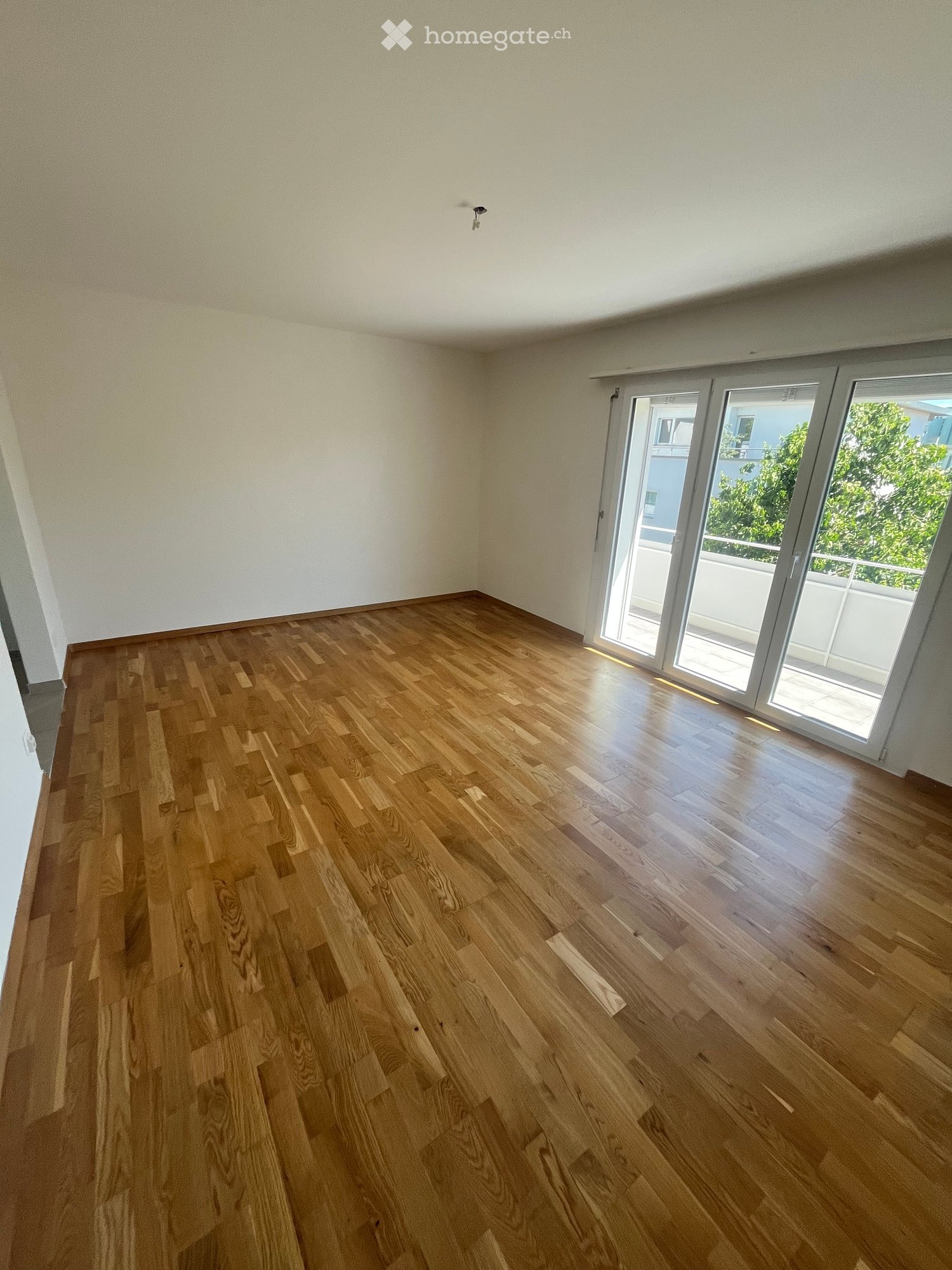 Empty room with light wooden flooring and large sliding glass doors leading to a balcony.